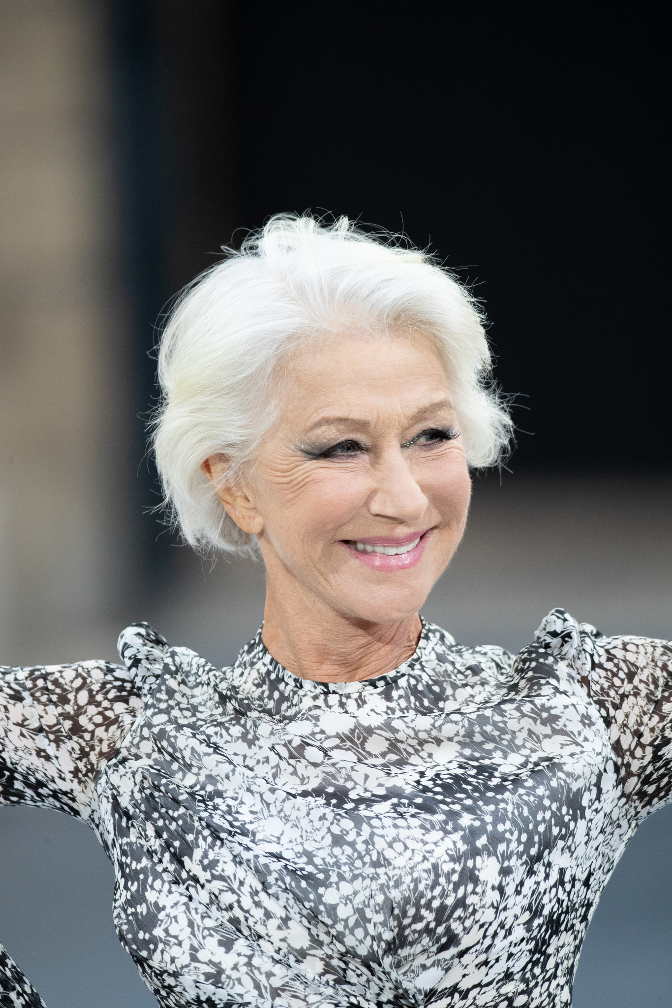 Smiling elderly woman with white hair wearing a black and white floral patterned top.